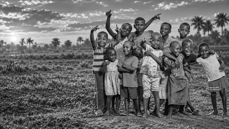 A group of smiling children waving in a rural field at sunset